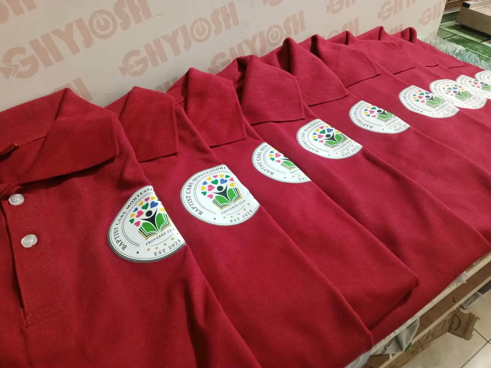 A row of red polo shirts printed with a Montessori school mark